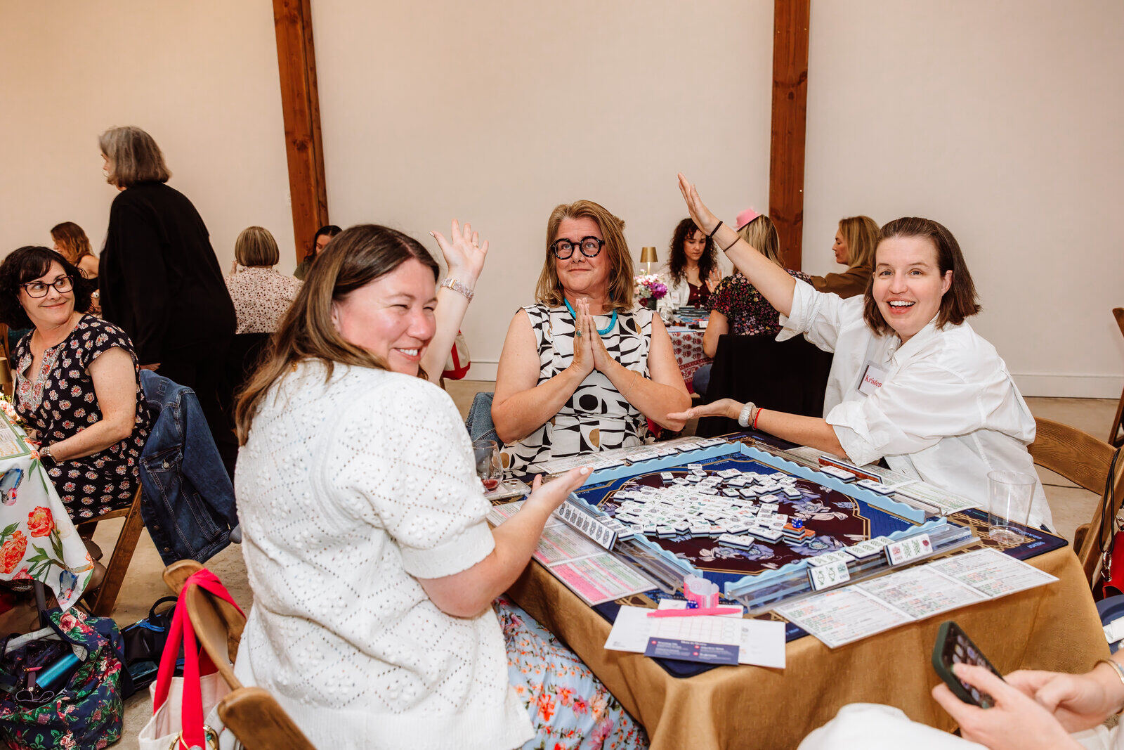 Players laughing around a mahjong table at an Open Play night